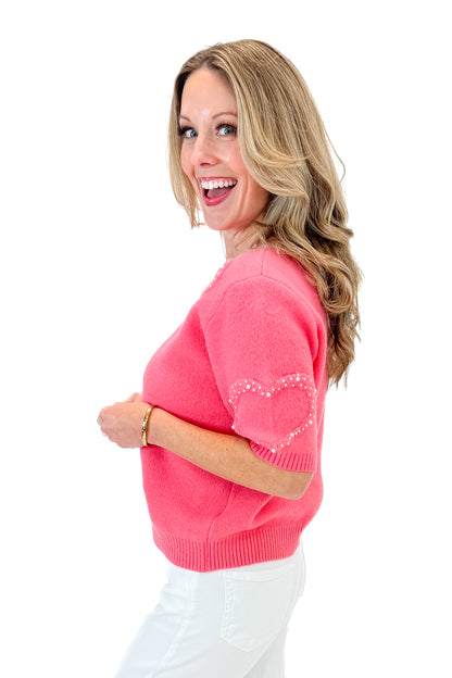 Side view of woman wearing Pink With Pearl Heart Detail Sweater with jeans against white studio background. 
