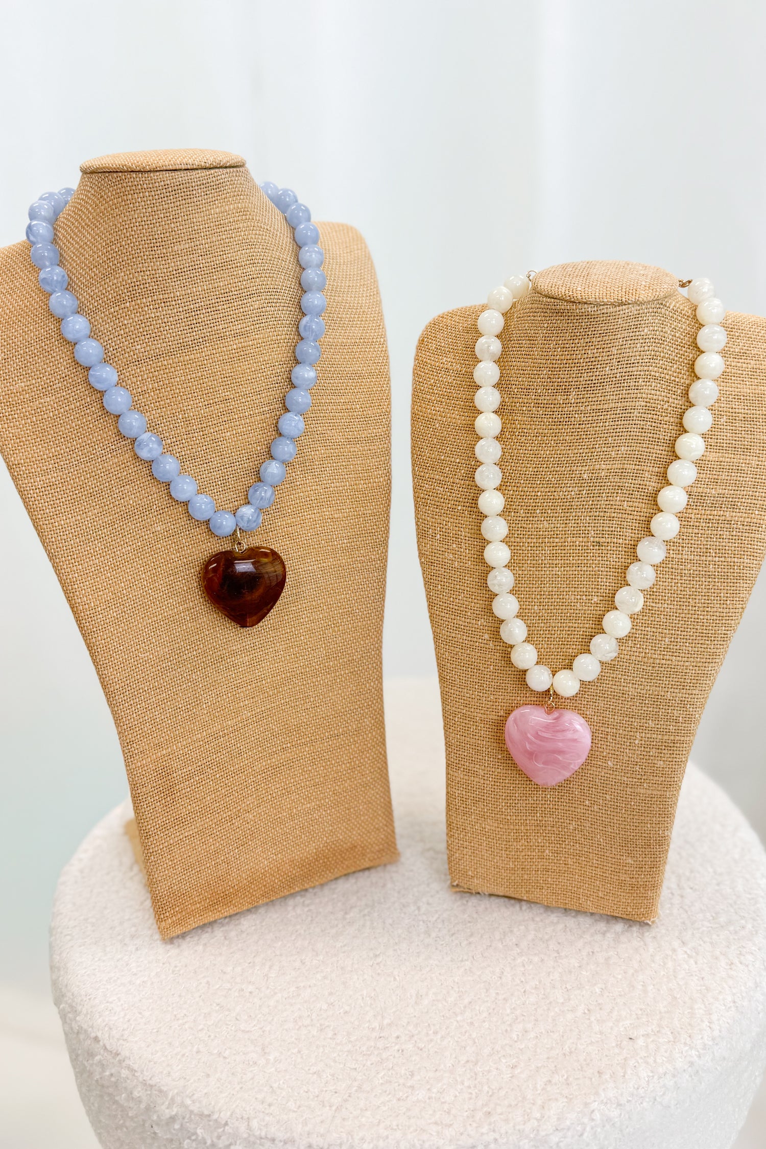 Two necklaces on mannequin busts with heart-shaped pendants against a white background