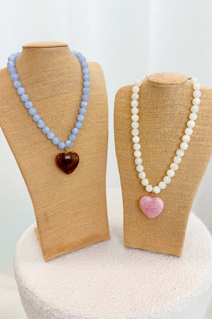 Two necklaces on mannequin busts with heart-shaped pendants against a white background
