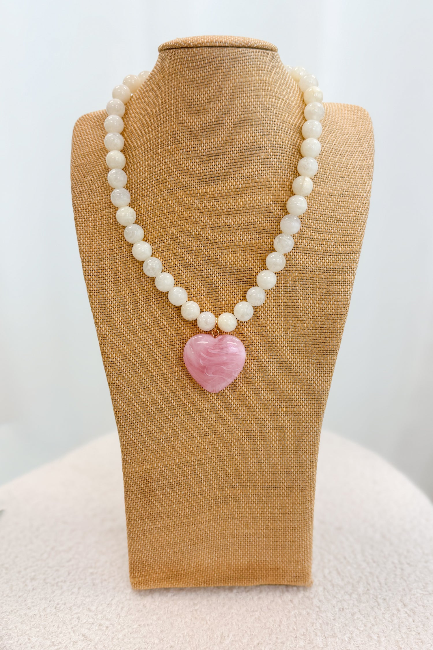 Necklace with a pink heart pendant on a beige mannequin bust against a white background