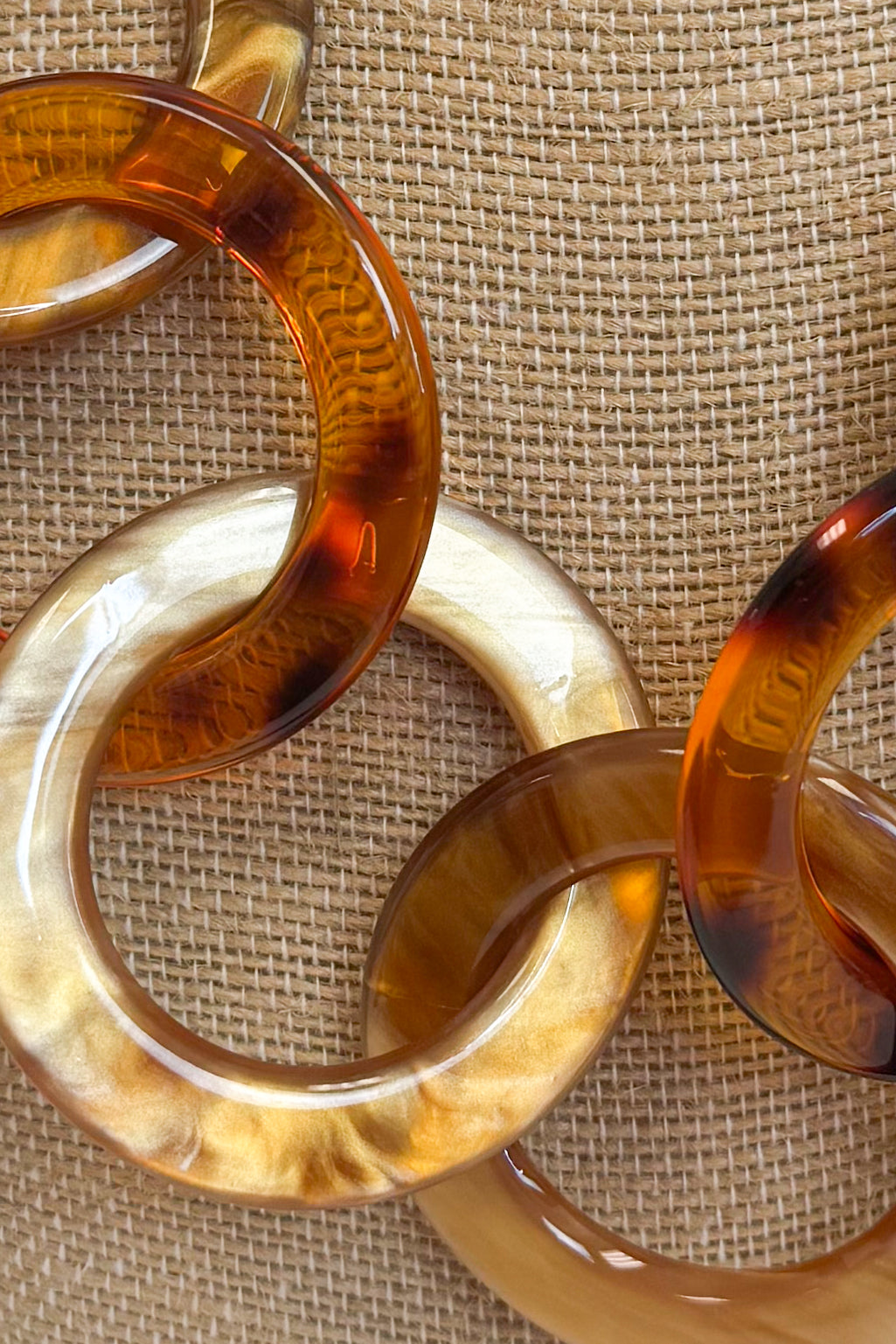 A close-up of translucent amber and cream interlocking circular links arranged on a textured beige fabric background.