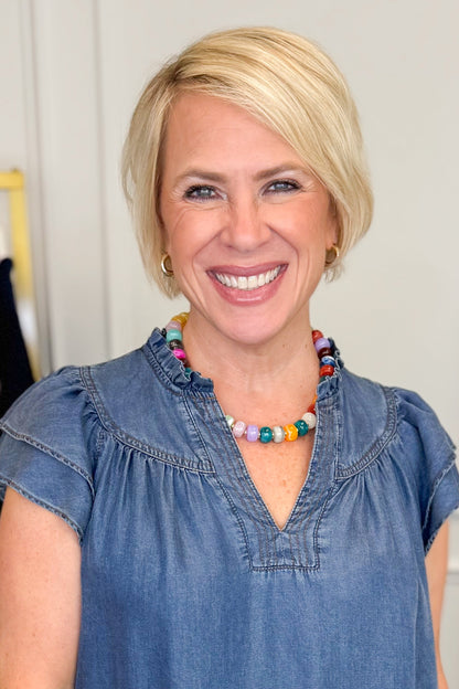 woman wearing a denim shirt and colorful beaded necklace against a white background