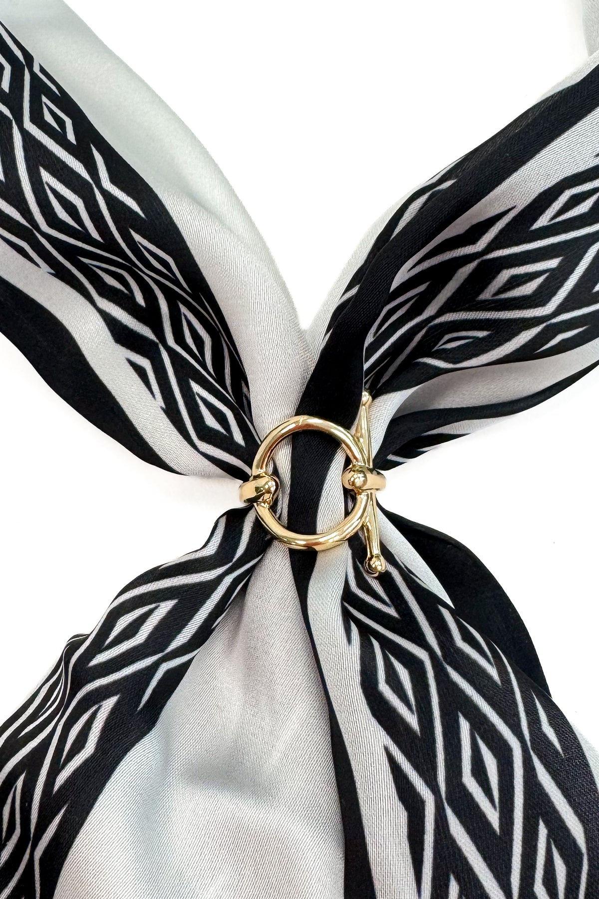 A close-up of a black and white patterned silk scarf tied in a knot with a gold ring clasp, set against a plain white background.