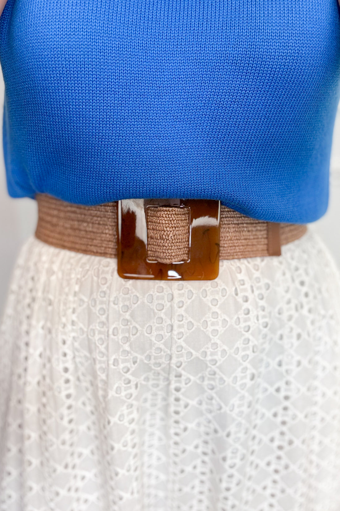 Blue top and white skirt with a brown belt on a neutral background