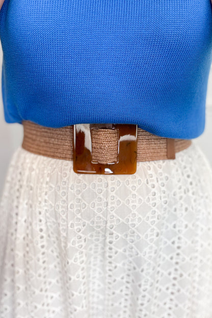 Blue top and white skirt with a brown belt on a neutral background
