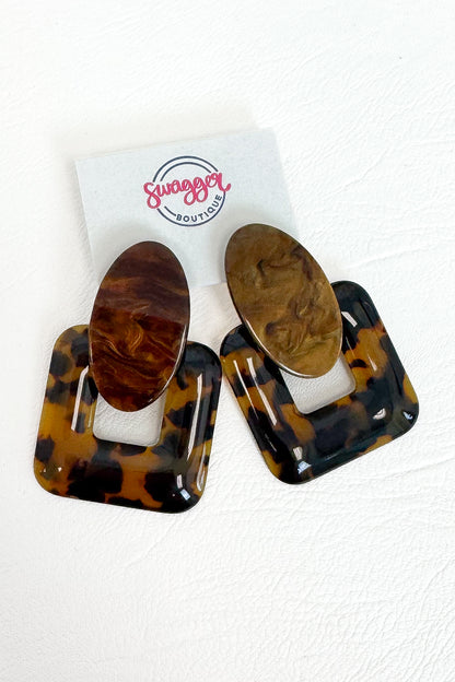 A pair of large square and oval drop earrings in glossy tortoiseshell and wood-grain patterns, displayed on a white card with the &