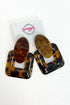 A pair of large square and oval drop earrings in glossy tortoiseshell and wood-grain patterns, displayed on a white card with the &