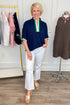 Woman in navy top with green and white accents and white pants standing in a clothing store.