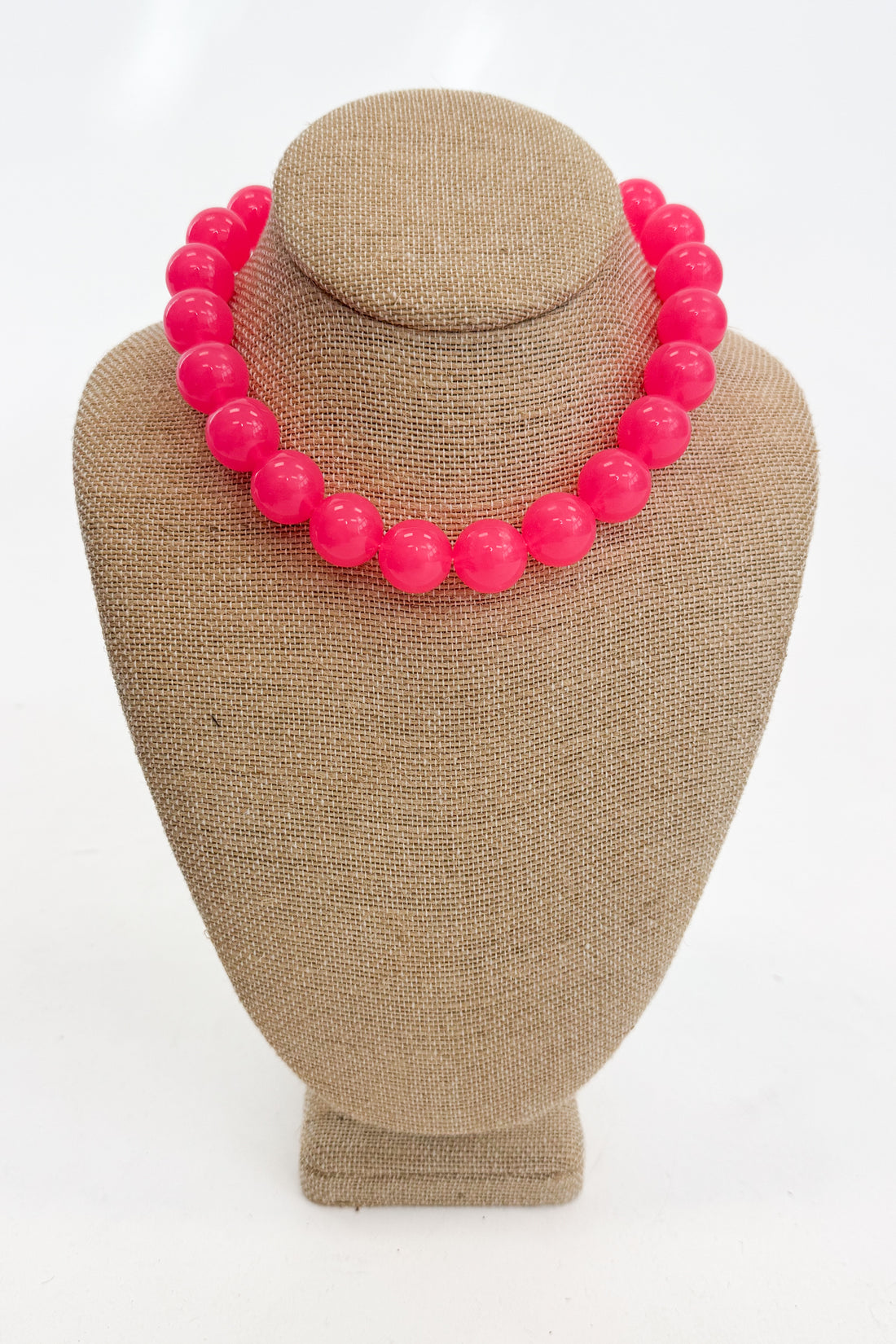 Necklace with bright pink beads on a beige mannequin bust against a white background