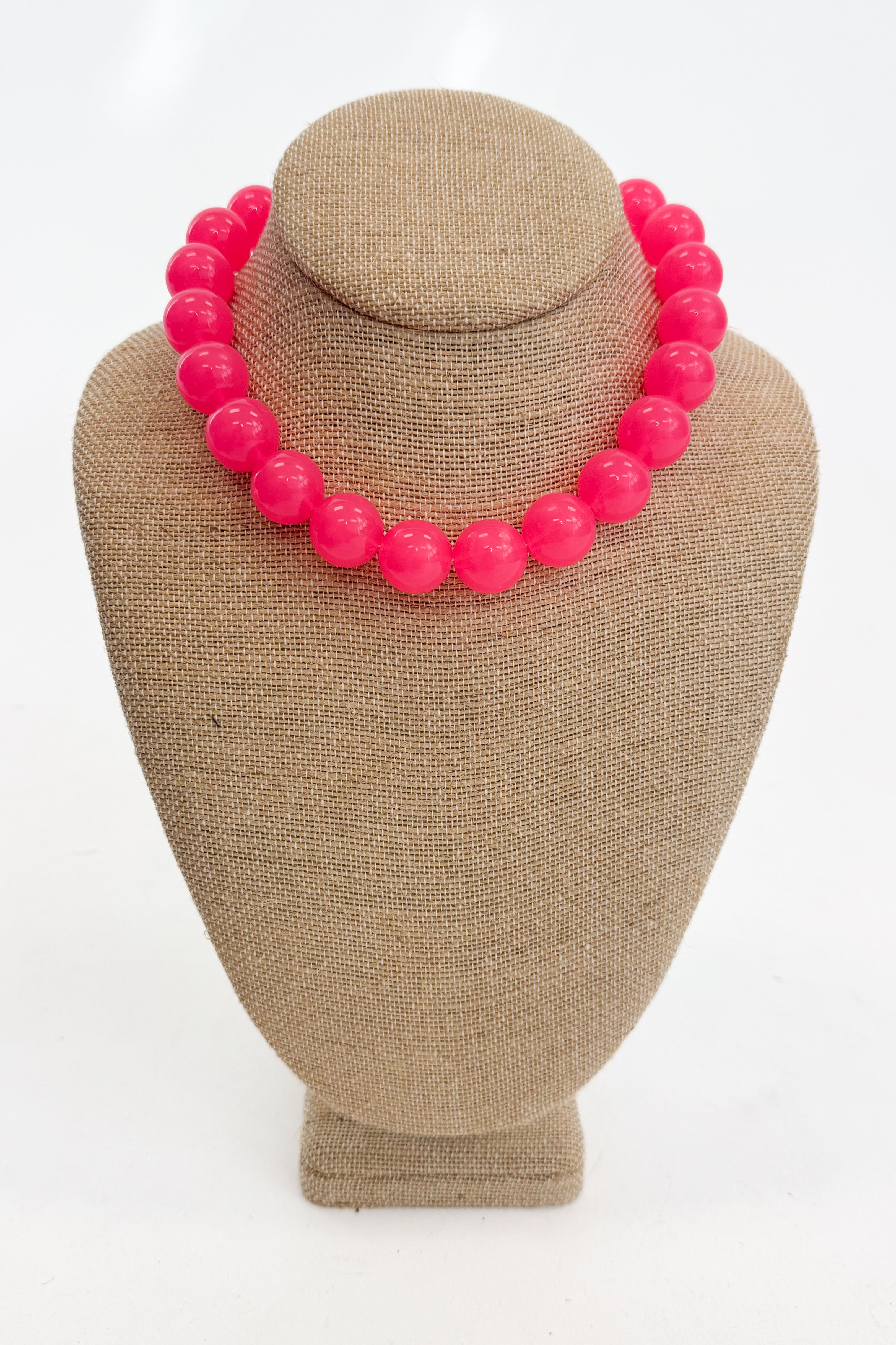 Necklace with bright pink beads on a beige mannequin bust against a white background