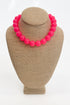 Necklace with bright pink beads on a beige mannequin bust against a white background