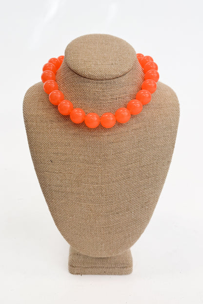 Neon orange beaded necklace on a brown mannequin bust against a white background