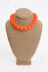 Neon orange beaded necklace on a brown mannequin bust against a white background