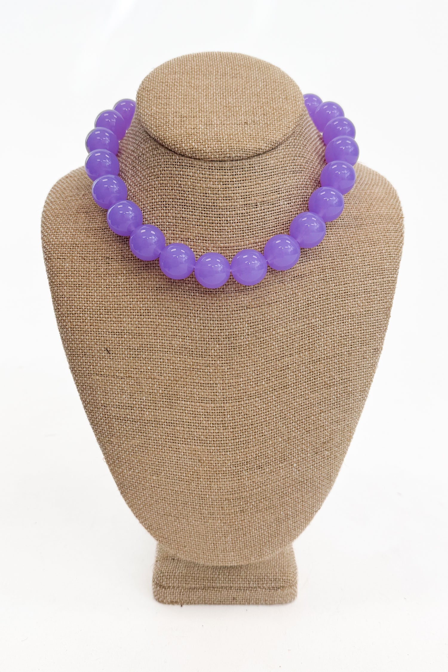 Purple beaded necklace on a brown mannequin bust against a white background
