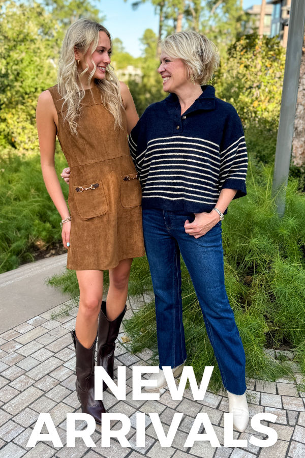 Two women standing outdoors on a paved walkway with greenery in the background. The woman on the left wears a sleeveless brown suede-like mini dress with front pockets and dark brown cowboy boots.