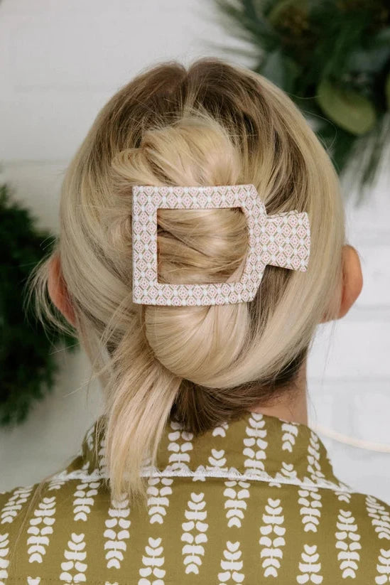 Person with blonde hair styled in a bun with a decorative hair clip, wearing a green patterned garment.