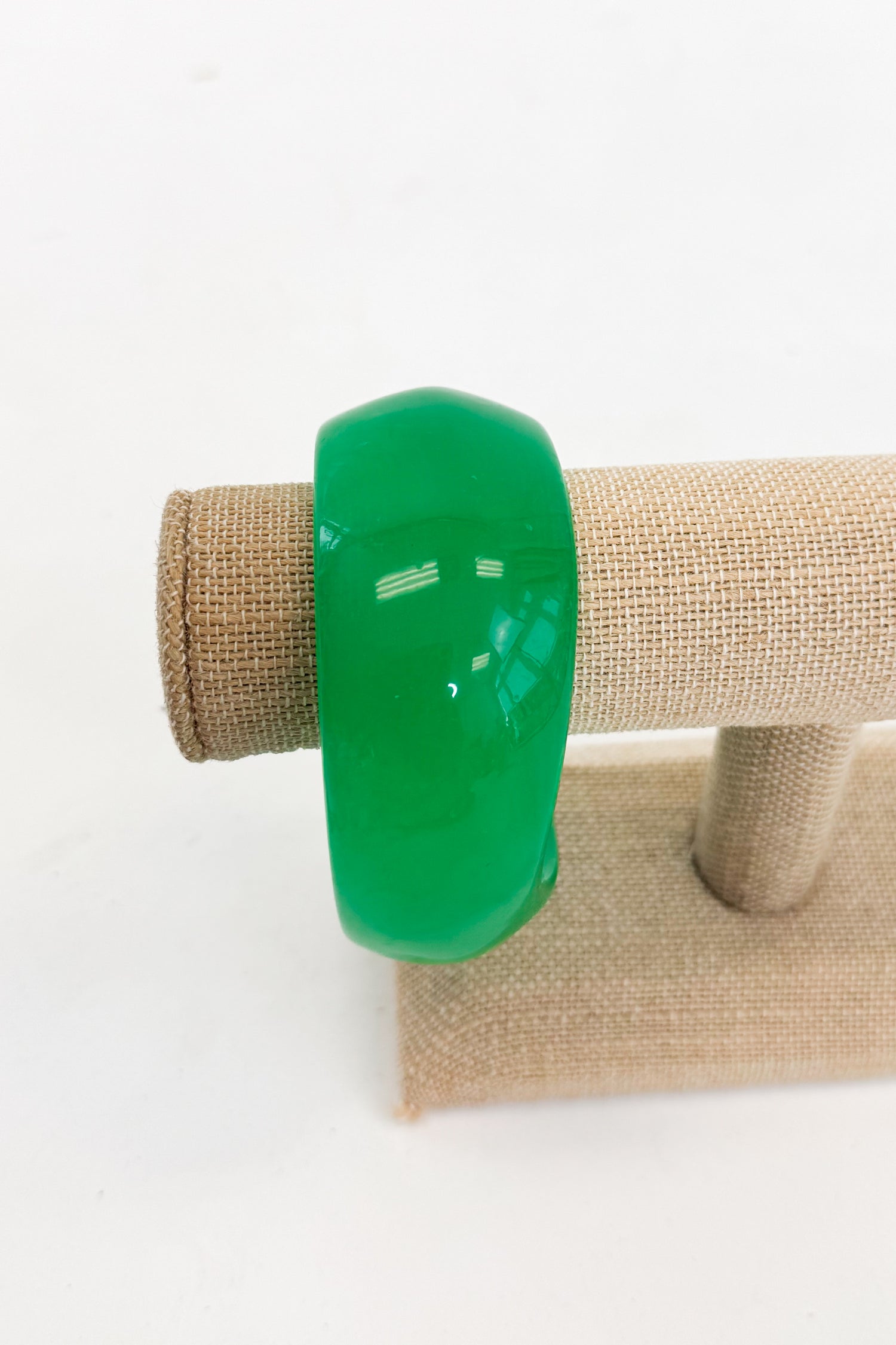 Green bracelet on a beige jewelry display stand against a white background