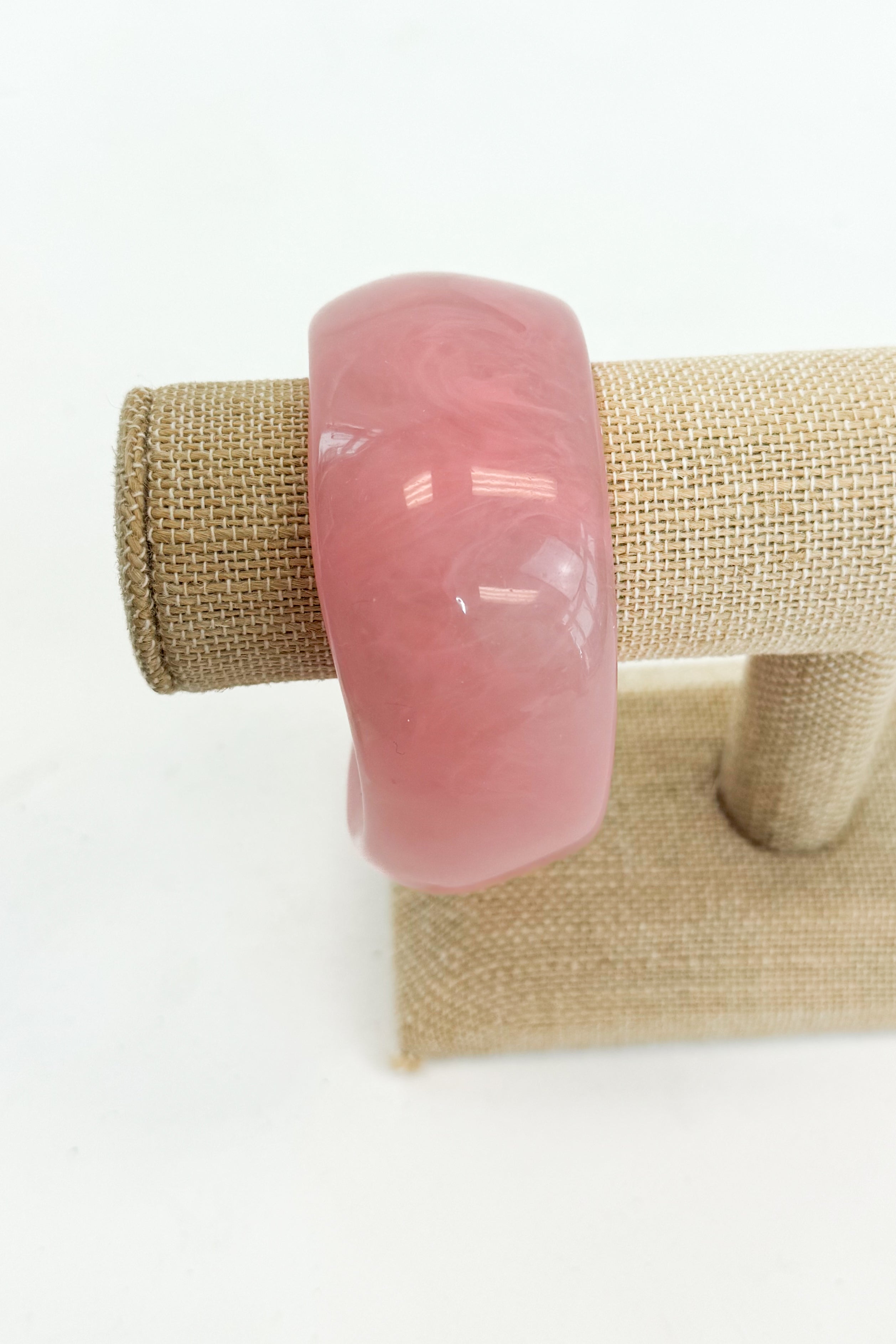 Pink bangle on a beige jewelry display stand with a white background