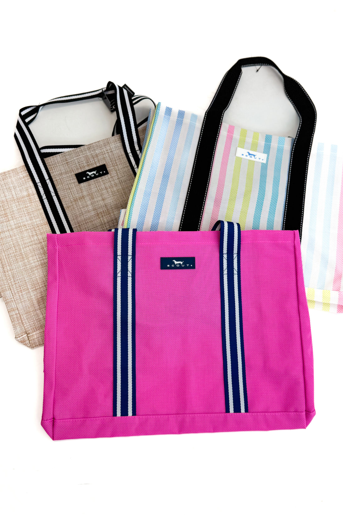 Collection of bags including a pink tote with striped handles on a white background