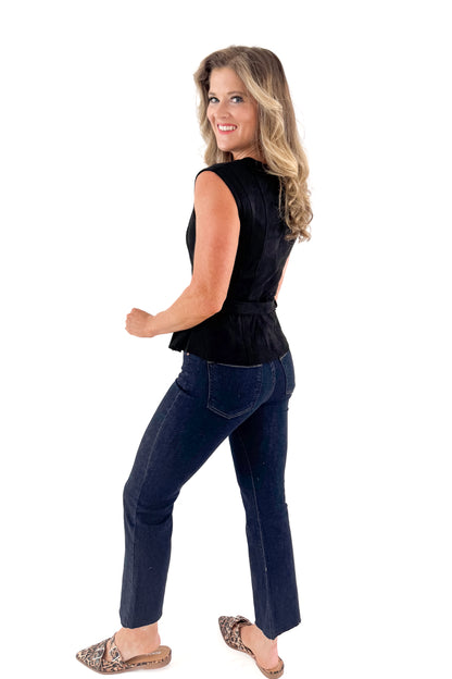 Side view of woman wearing Black Suede Belted Peplum Top with jeans against white studio background.