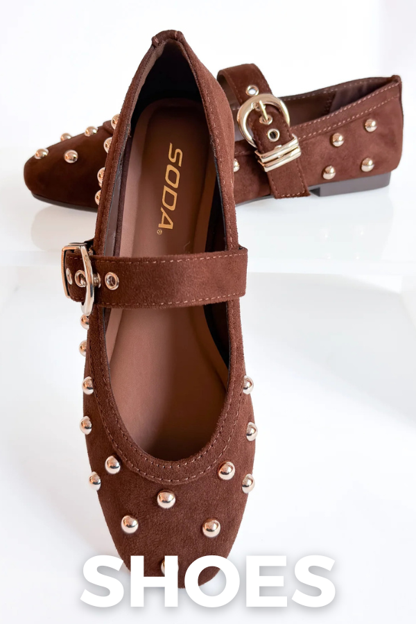 A pair of brown suede flat shoes with gold-tone buckle straps and metal studs, displayed on a white reflective surface. The brand name 'SODA' is visible on the insole of the front shoe.