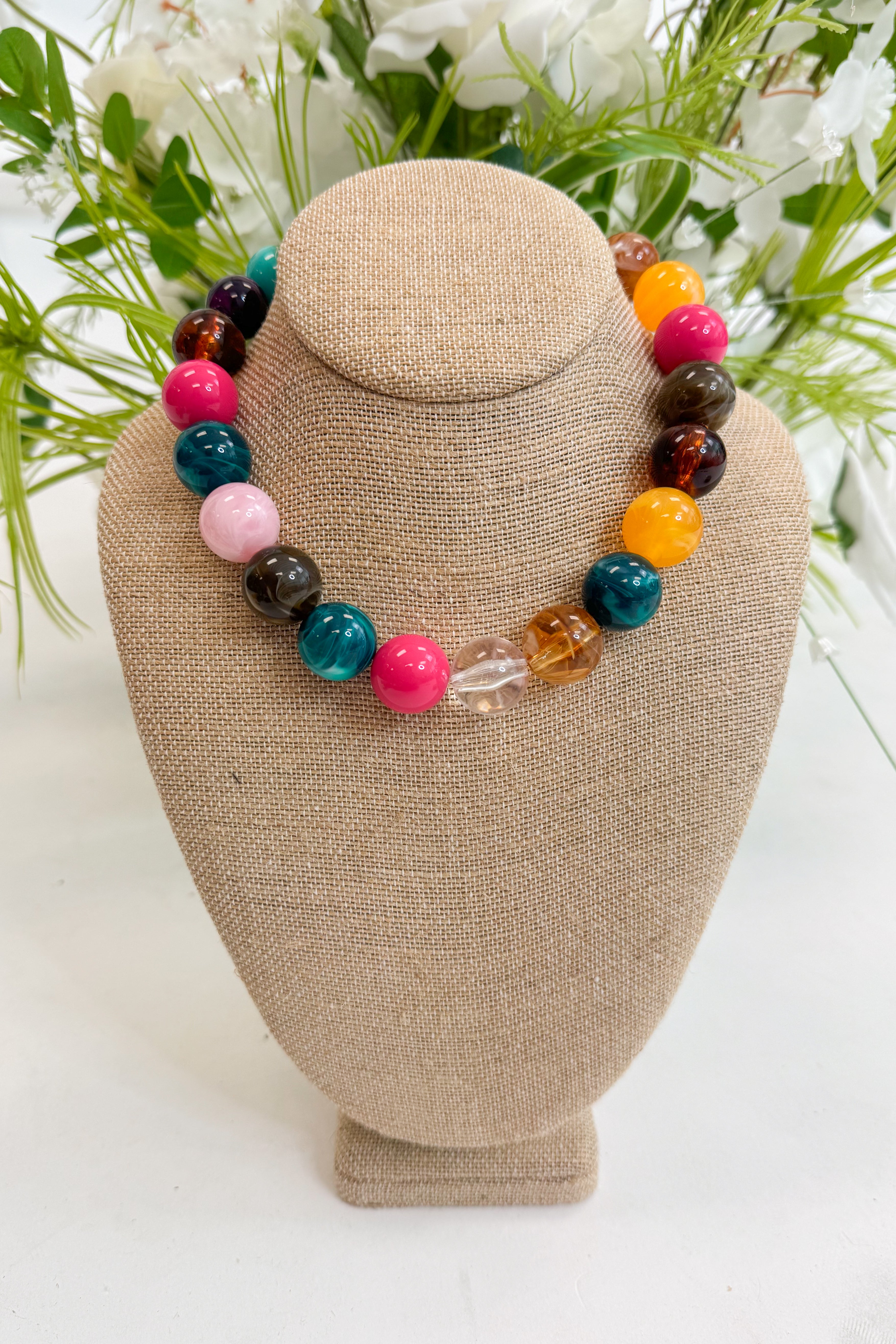 Colorful beaded bracelet on a beige jewelry display with greenery in the background