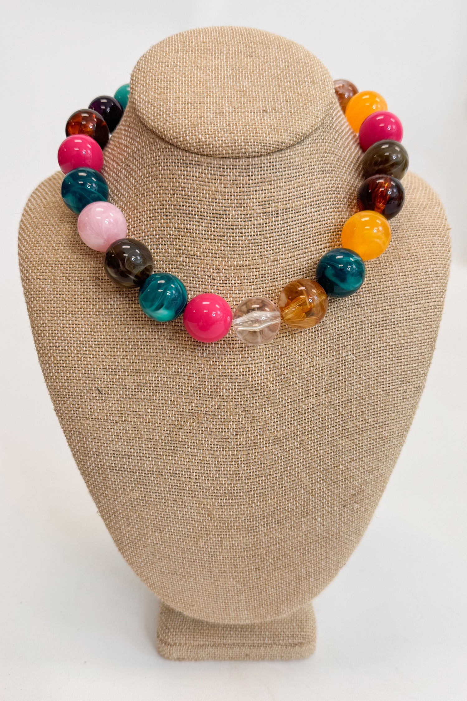 Colorful beaded necklace on a beige jewelry display stand against a white background