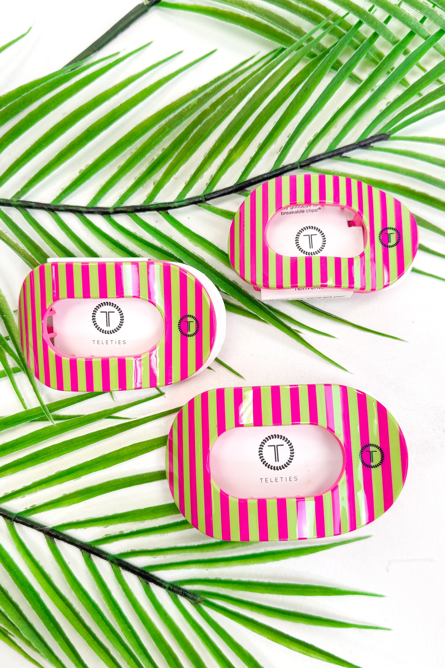 Three pink and green striped hair clips on a white background with palm leaves.