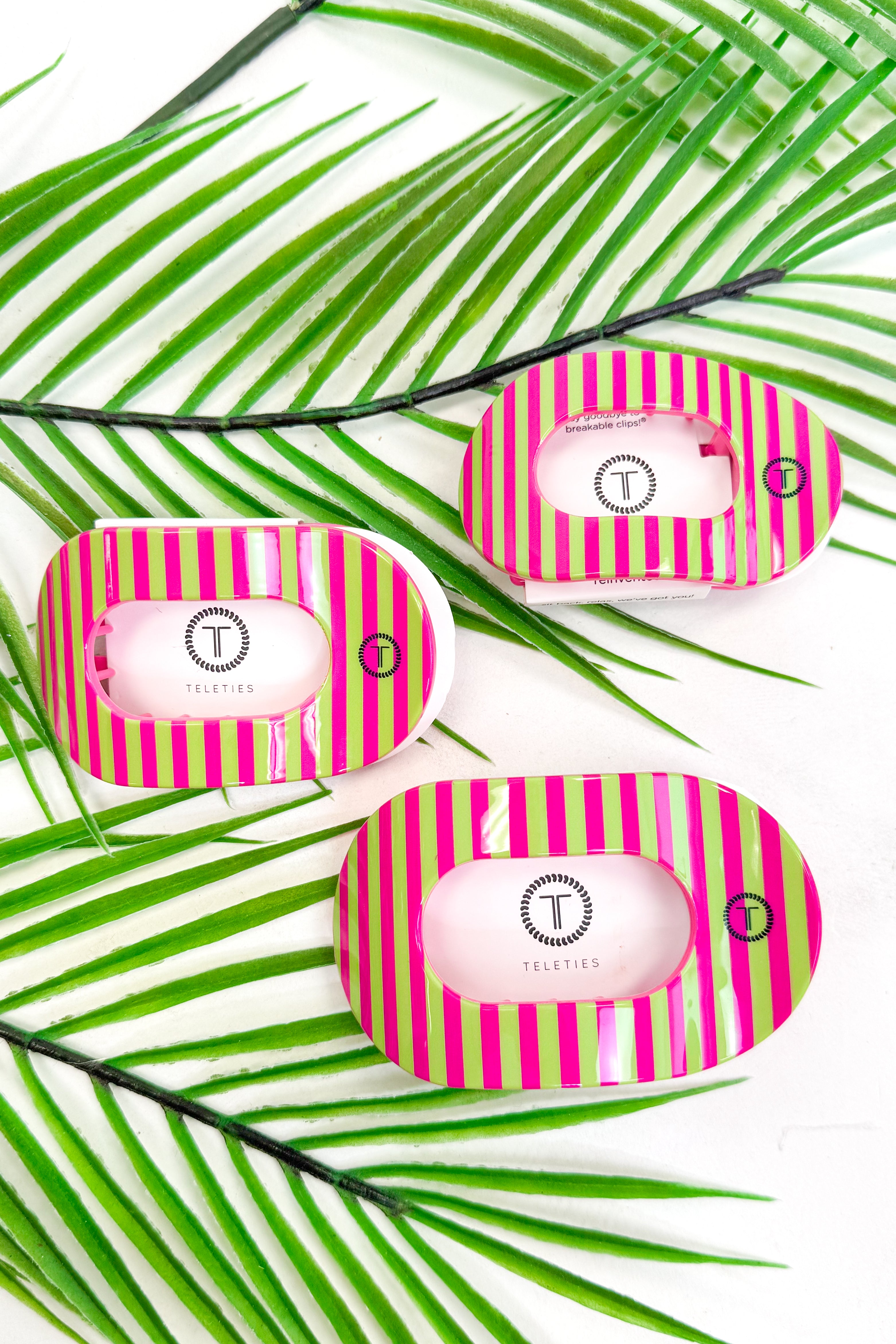 Three pink and green striped hair clips on a white background with palm leaves.