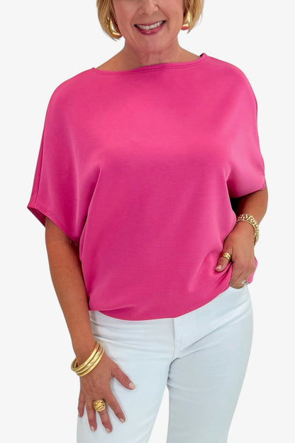 Woman wearing a bright pink top and white pants on a white background