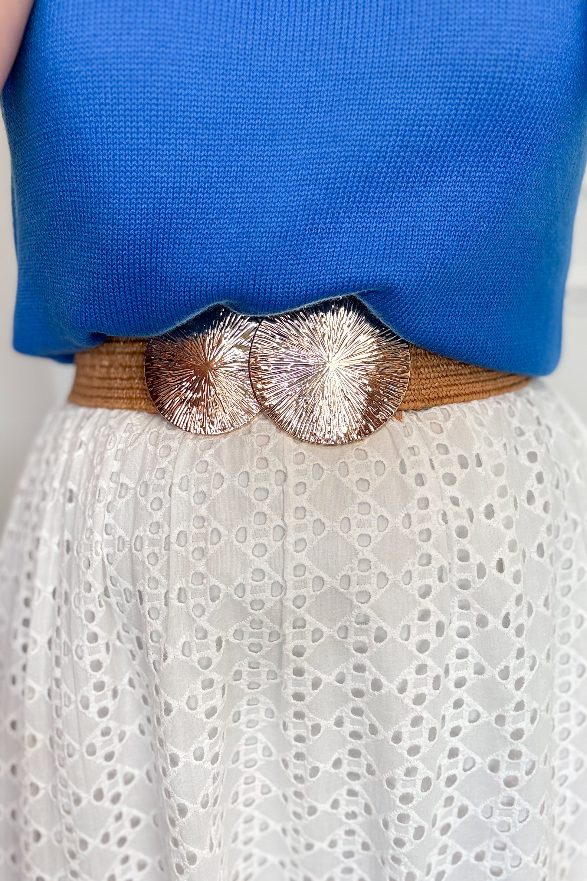 Close-up of a person wearing a brown belt with decorative elements over a blue top and white lace garment.