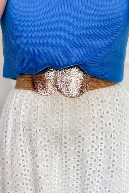 Close-up of a person wearing a brown belt with decorative elements over a blue top and white lace garment.