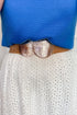 Close-up of a person wearing a brown belt with decorative elements over a blue top and white lace garment.