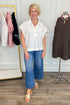 Woman in a white blouse and blue jeans standing in a clothing store with racks and mannequins in the background.