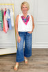 Woman wearing a colorful scarf, white top, blue jeans, and gold sandals in a room with a clothing rack.