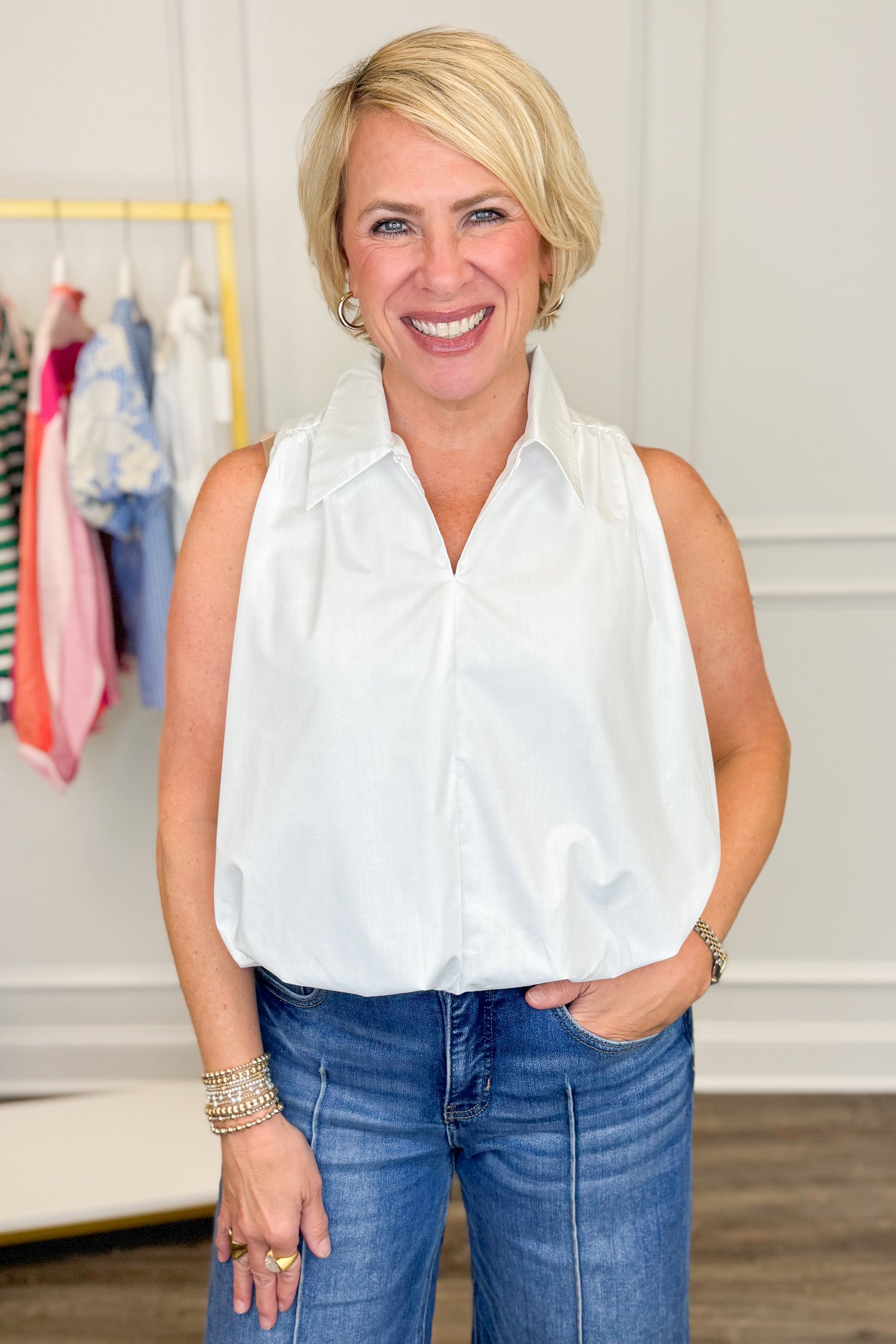 Woman wearing a white sleeveless blouse and blue jeans in a clothing store.
