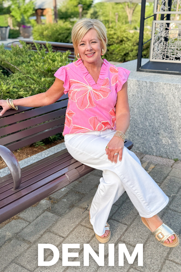 Woman in pink floral top and white pants sitting on a bench with 'Denim' text overlay.