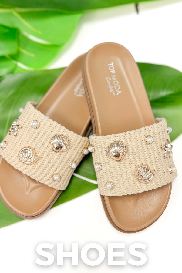 Beige sandals with shell and pearl embellishments on a green leaf background