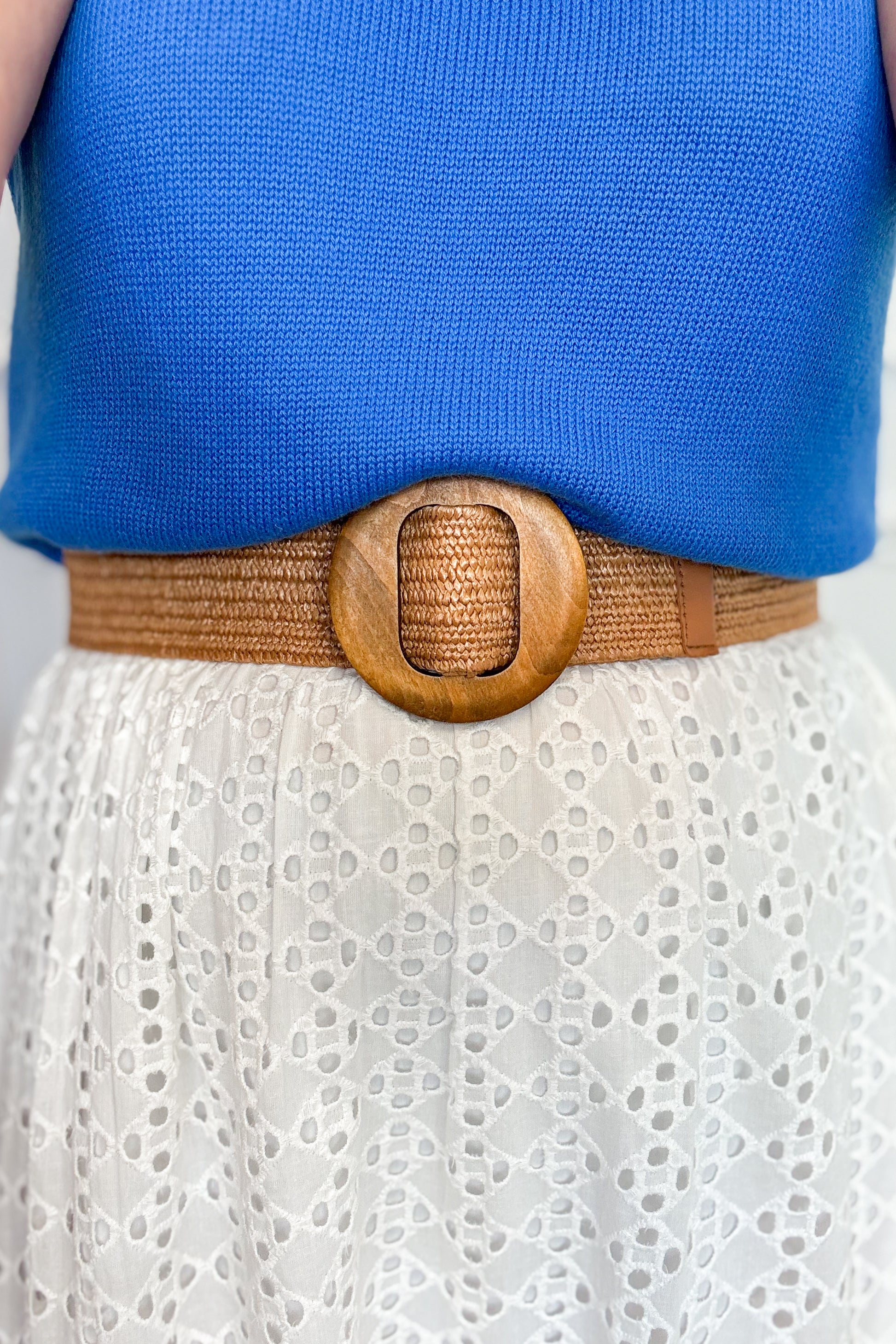 Person wearing a blue top and white lace skirt with a brown belt featuring a wooden buckle.