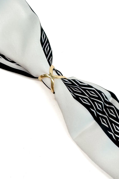 A white silk scarf with black geometric patterns, tied in a knot with a gold ring, on a white background.
